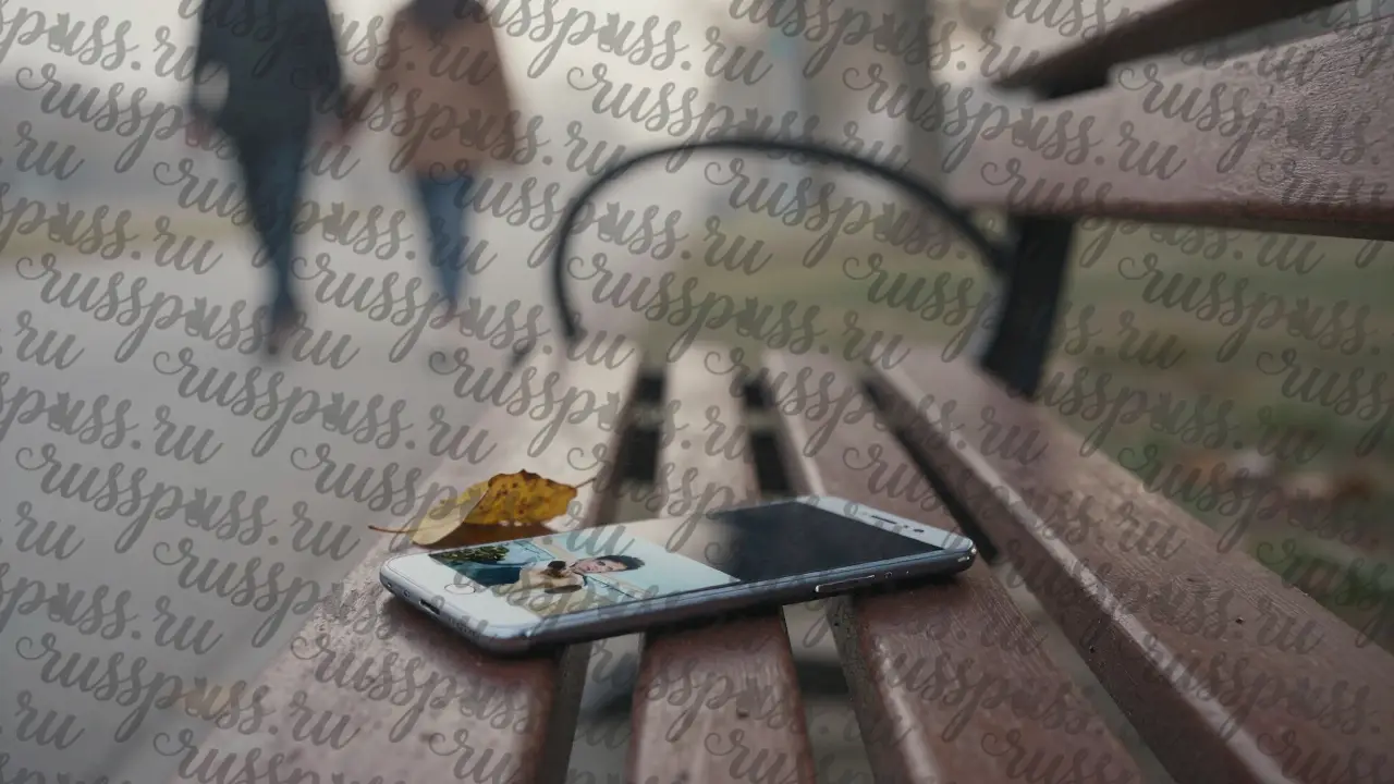 Пустая скамейка в парке утром, на ней лежит выключенный телефон с фото на экране.